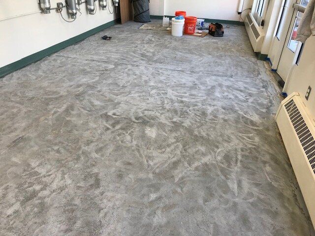 A concrete floor in a room with buckets and a radiator.