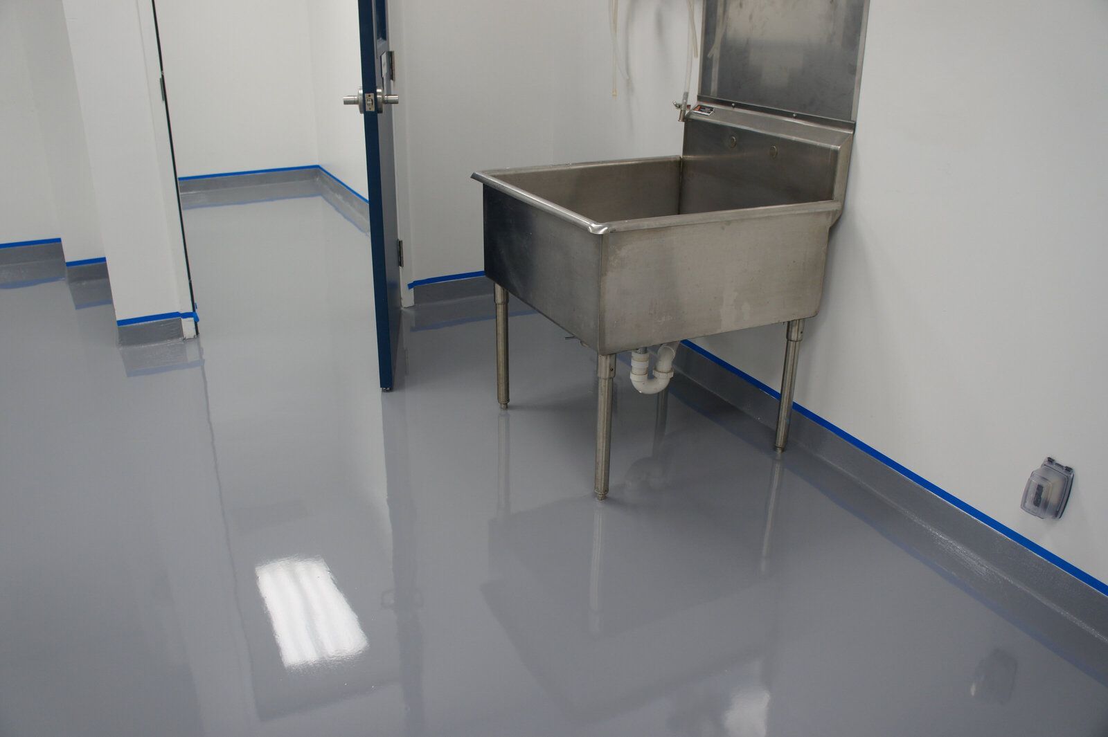 A stainless steel sink is sitting in a room next to a door.