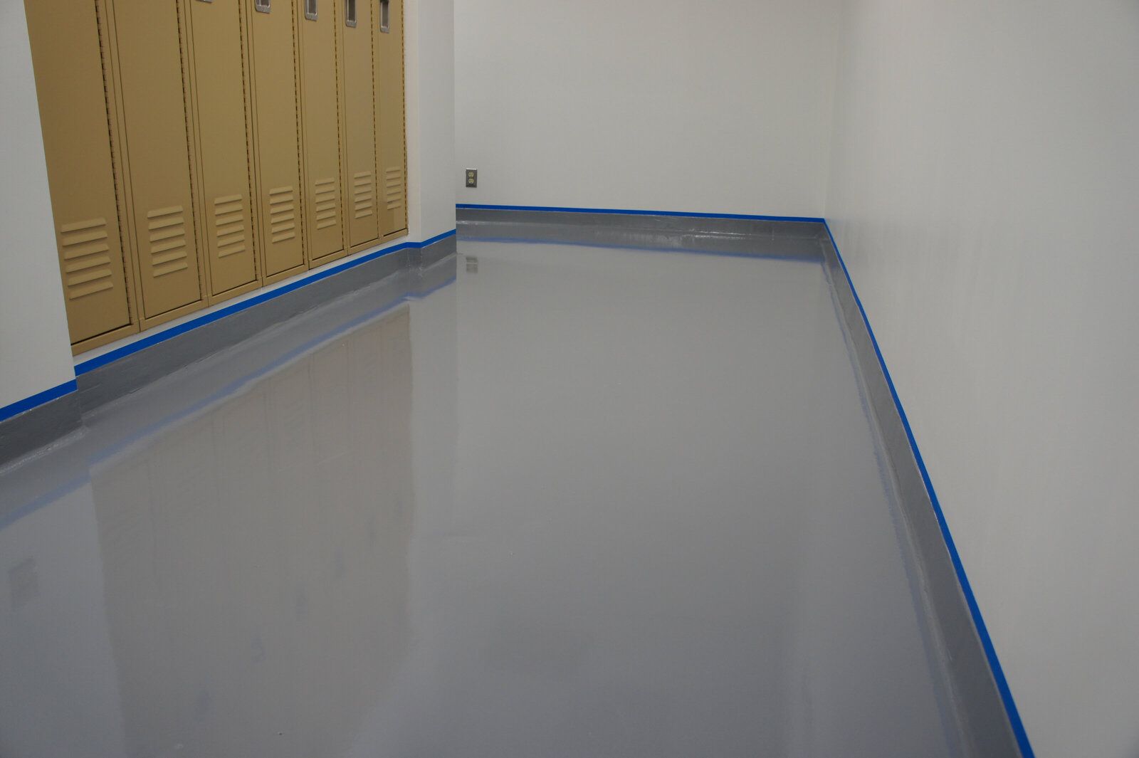 A room with lockers on the wall and a gray floor.