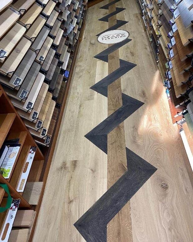 A bookstore aisle with wooden floor and black zigzag path markers between shelves