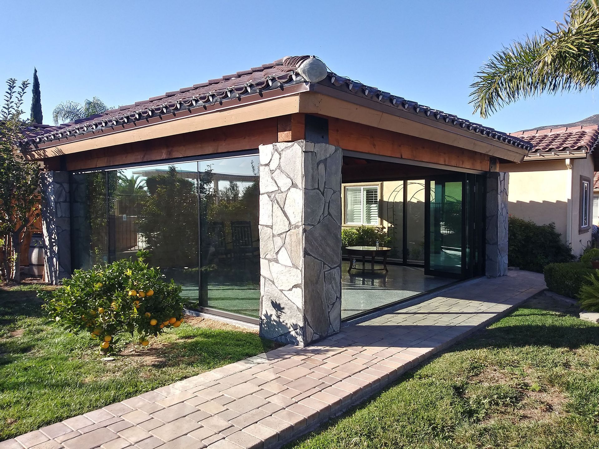 Covered patio with stone columns, glass walls, and a tiled roof.