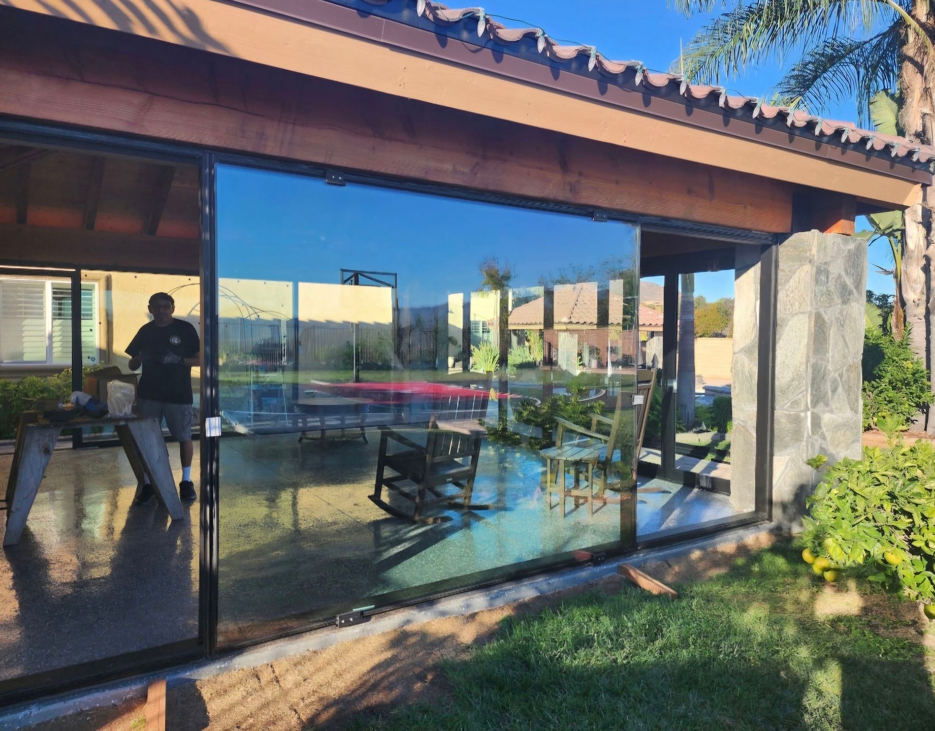 Exterior view of a patio with large glass doors reflecting a pool and yard. A person stands nearby.