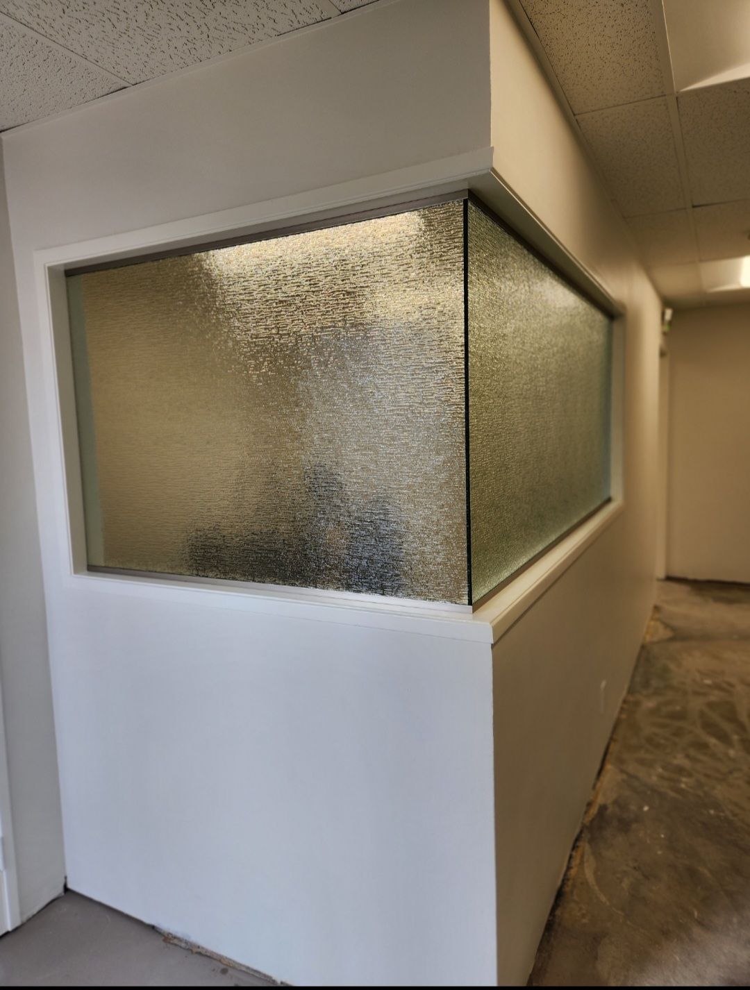 White walls with a textured glass window looking into a room. The hallway has a concrete floor.