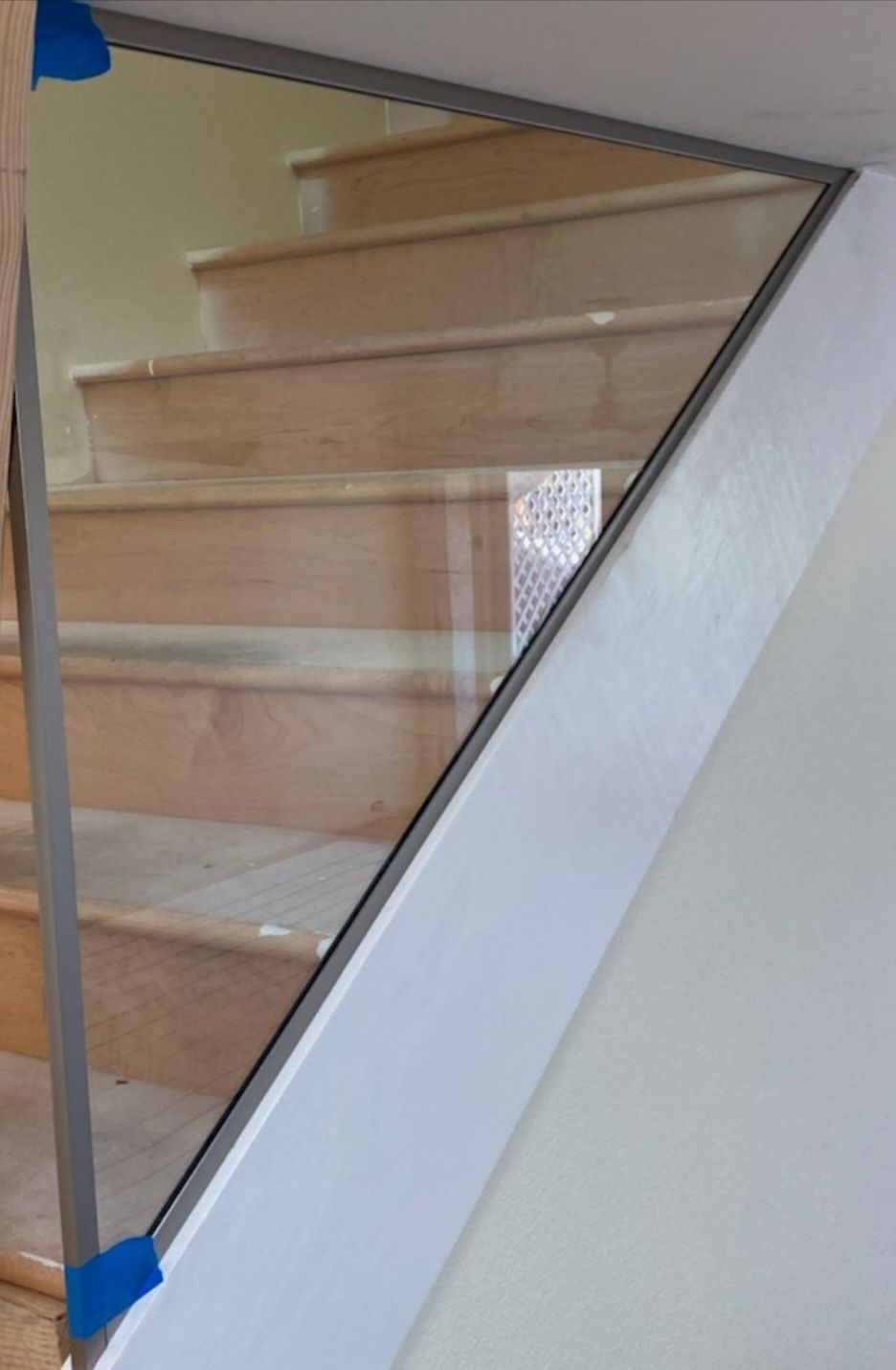Glass panel stair railing with gray metal frame and wooden stairs in background.