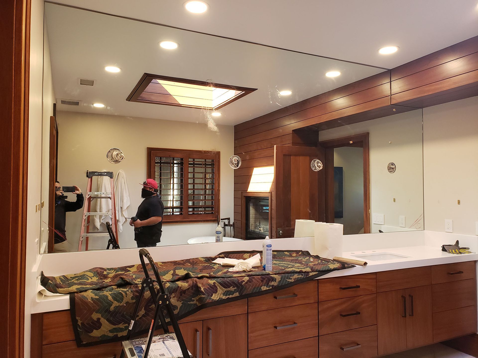 Bathroom with large mirrors, cabinets, and a person working on a ladder.