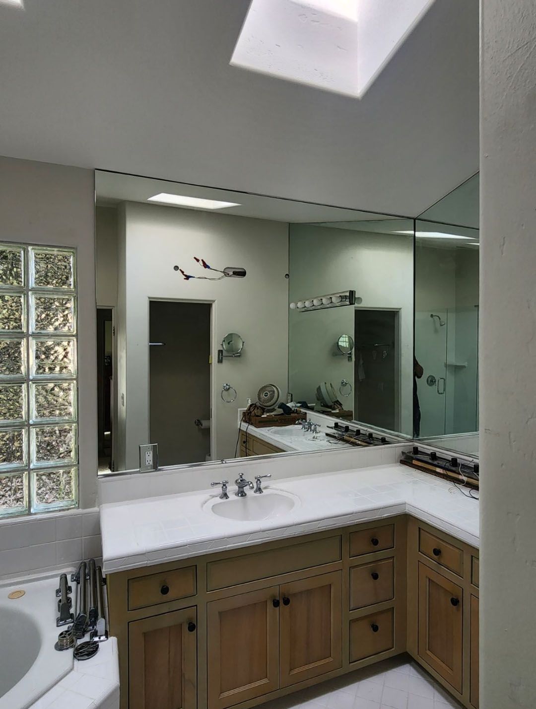 Bathroom with large mirror over a countertop with sink and wooden cabinets. Glass block window on the left.