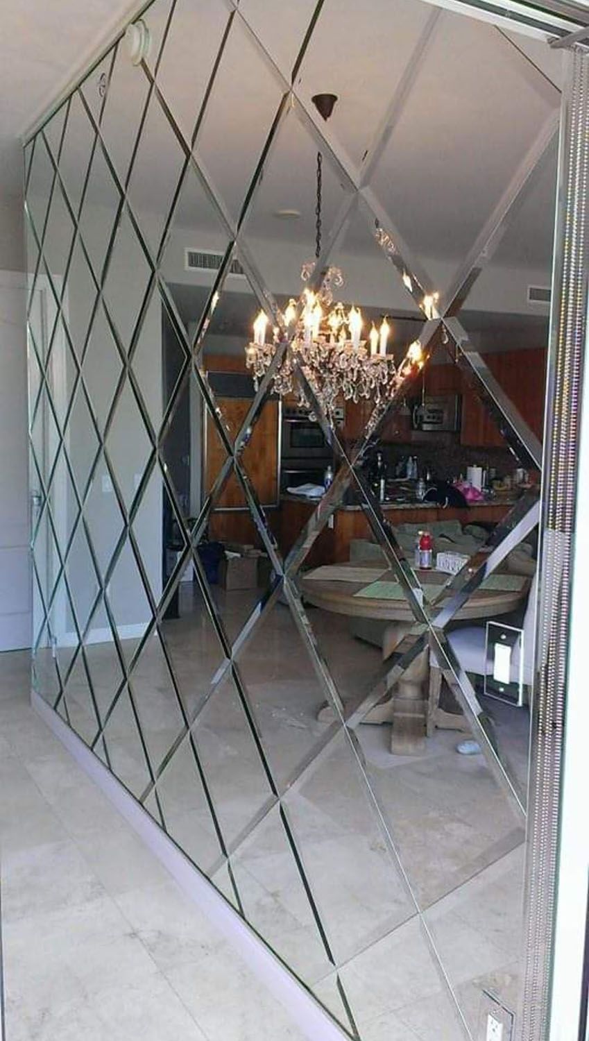 Mirrored wall panel with diamond pattern, reflecting a room with a chandelier and kitchen.