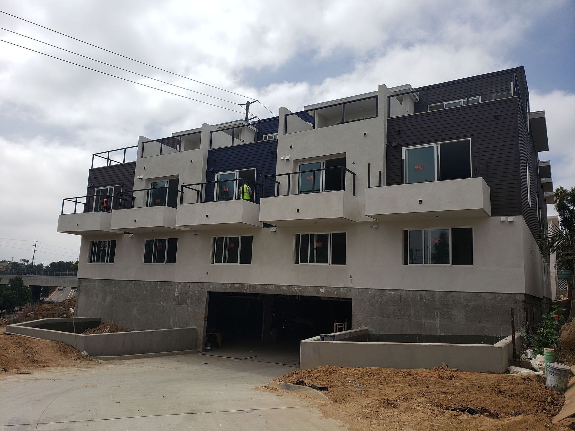 Multi-story apartment building under construction, exterior view. White, gray, and brown facade. Cloudy sky.