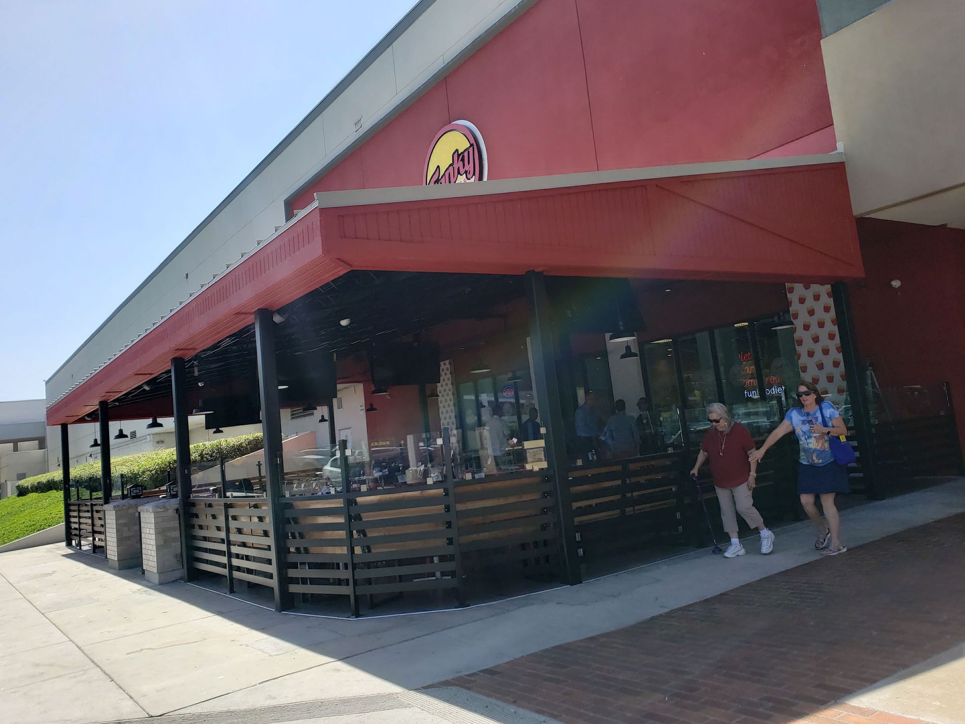 Restaurant with red awning and outdoor seating. People walk by.