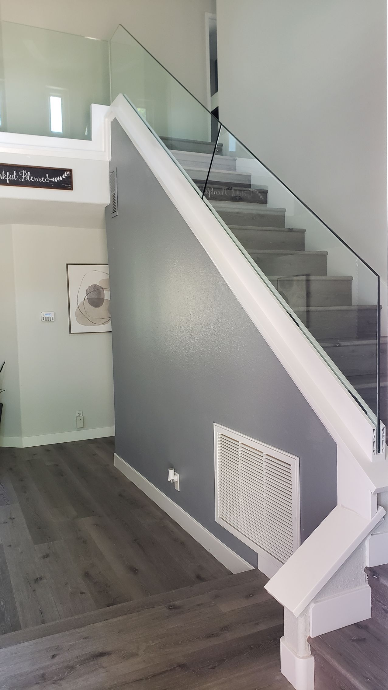 Staircase with glass railing, gray wall, and wood-look flooring. White trim accents the stairs and wall.
