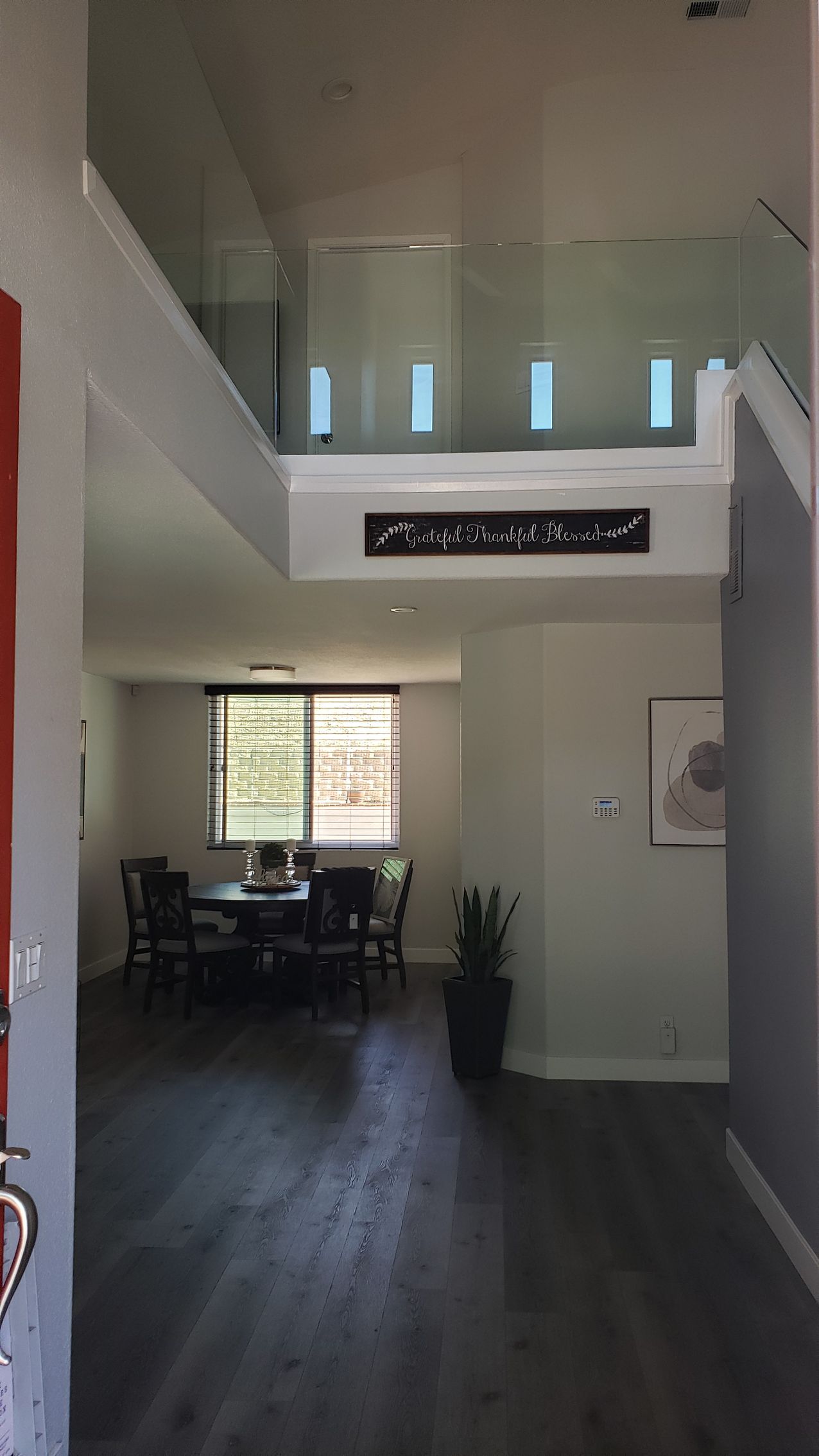 Entryway with dark wood floors, dining room, and second-story balcony with glass railing.