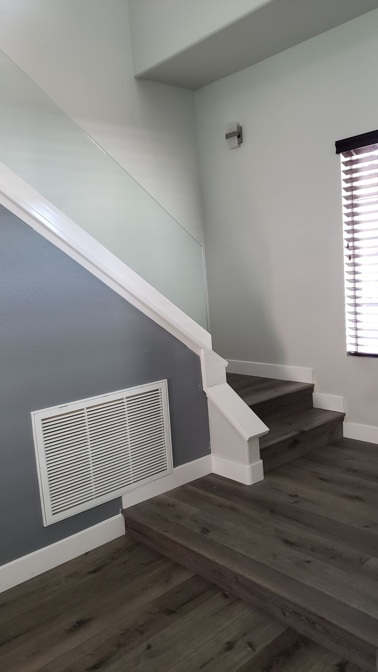 Staircase with gray and white walls. Dark wood-look steps and a vent on the left wall.