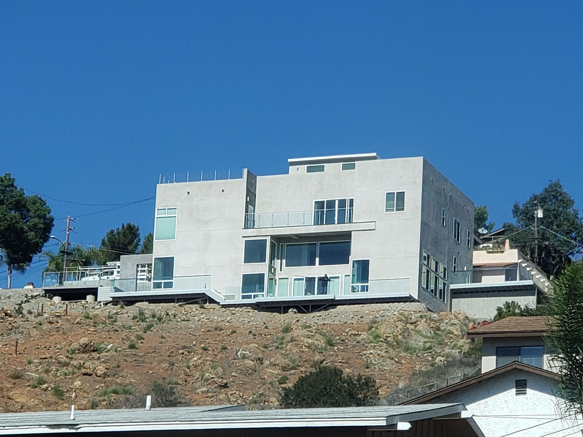 Modern house built on a hillside with large windows and balconies, under a blue sky.