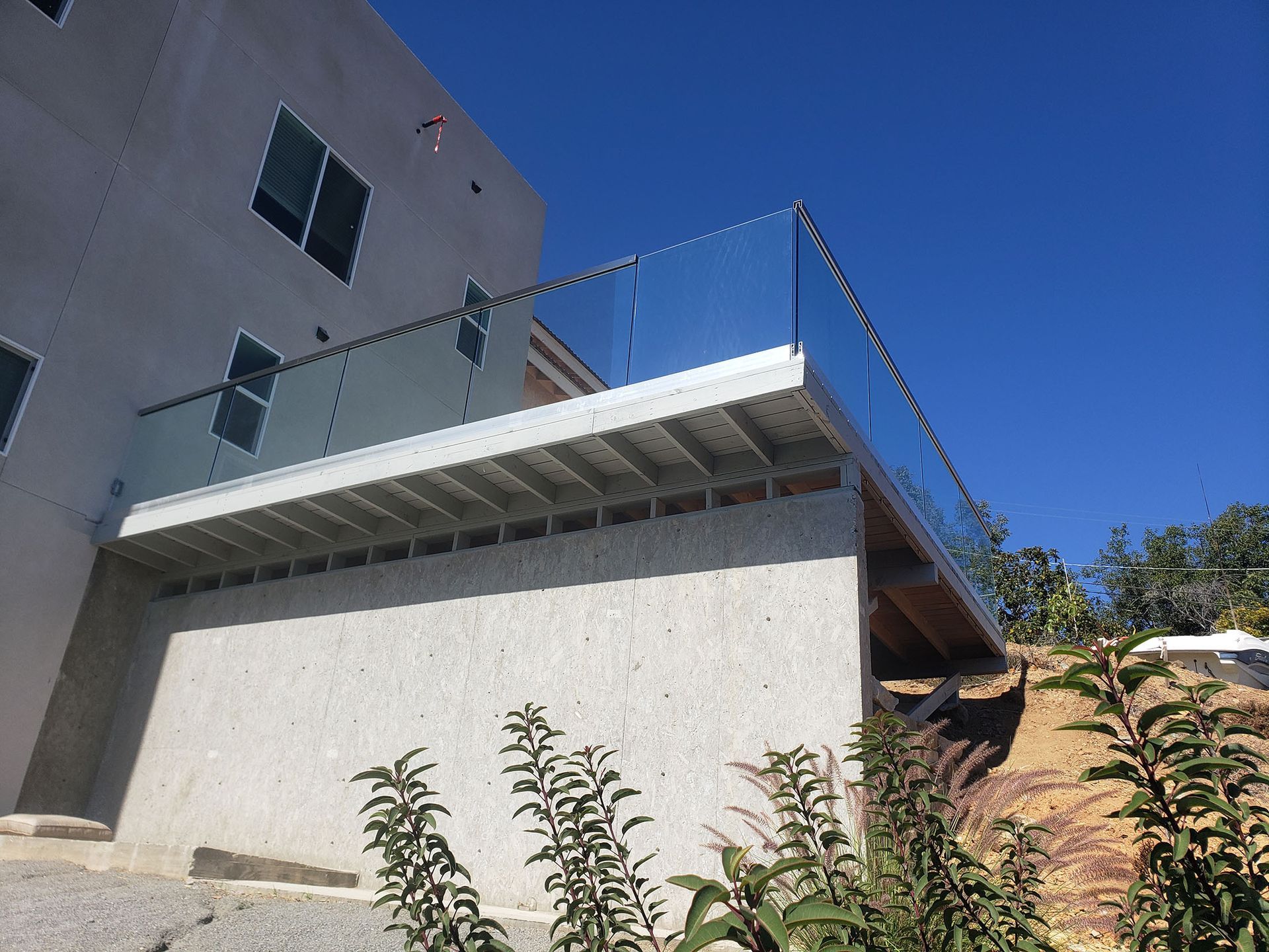 Modern deck with glass railing, attached to a light-colored building, under a blue sky.