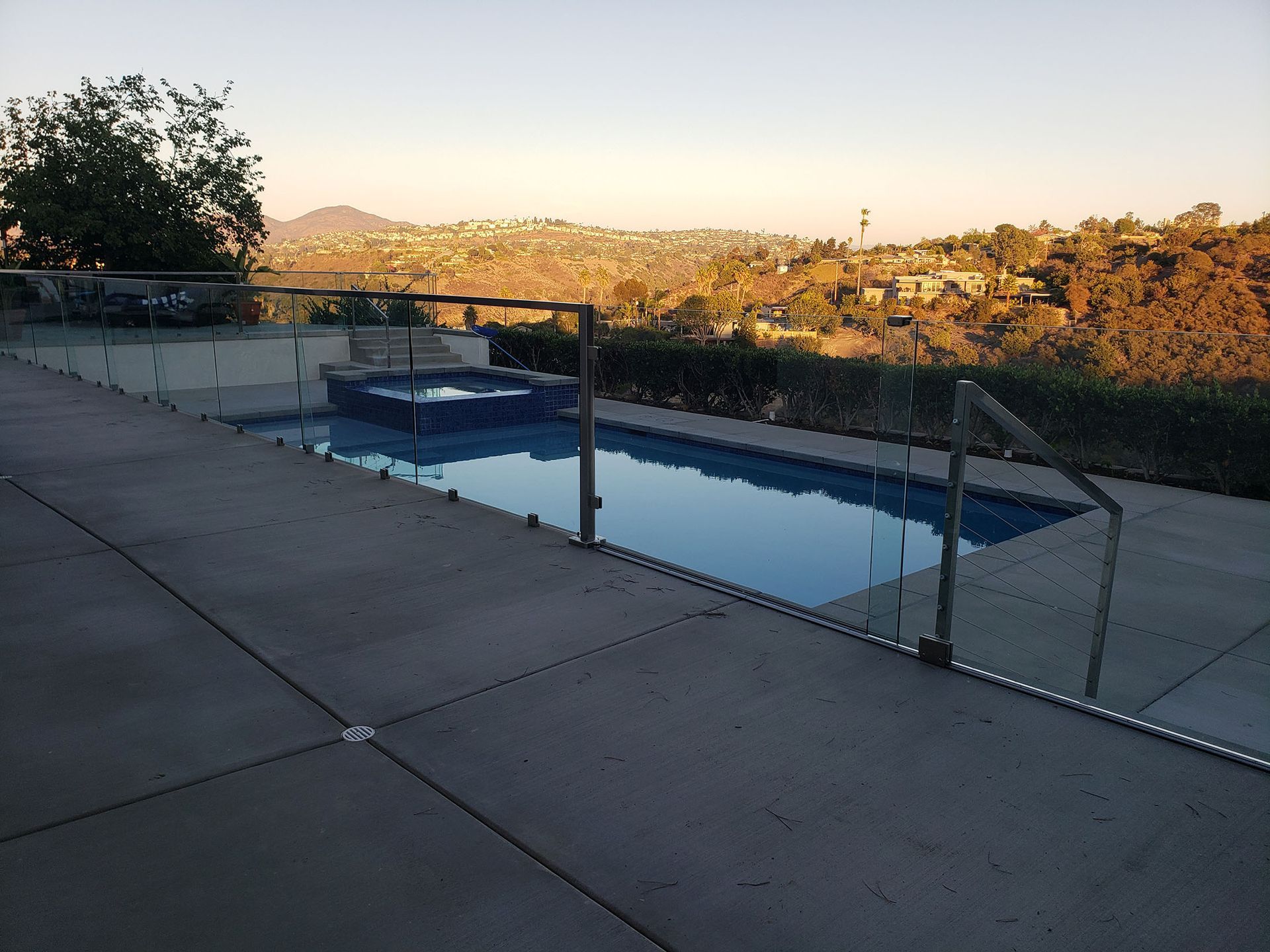 Pool with glass fence overlooking a scenic vista at dusk.