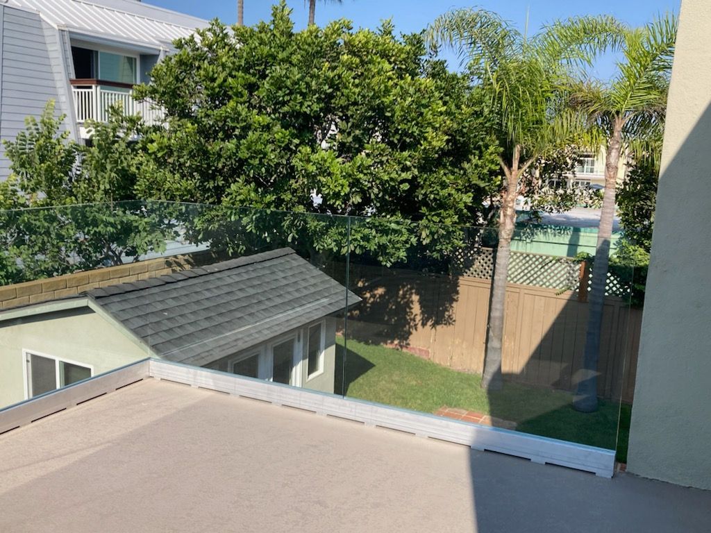 View from a balcony overlooking a small building with a green roof, trees, and a grassy backyard.