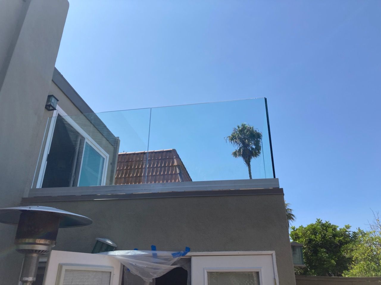 Glass railing on a rooftop patio with a blue sky background and a small palm tree.