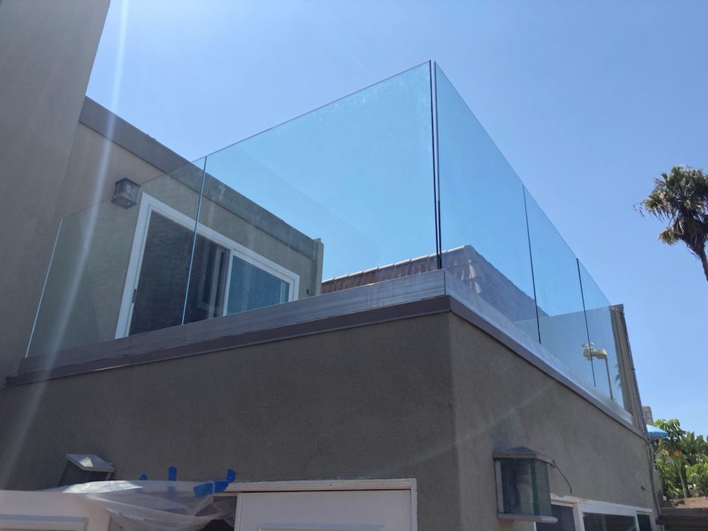 A rooftop with a glass railing against a clear blue sky.