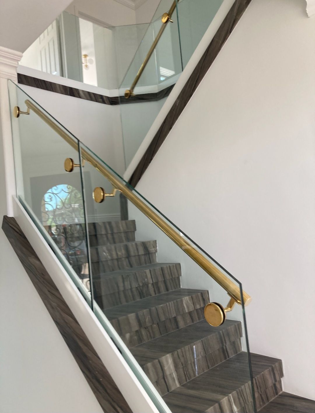 Staircase with glass and gold railing, brown steps, white walls.