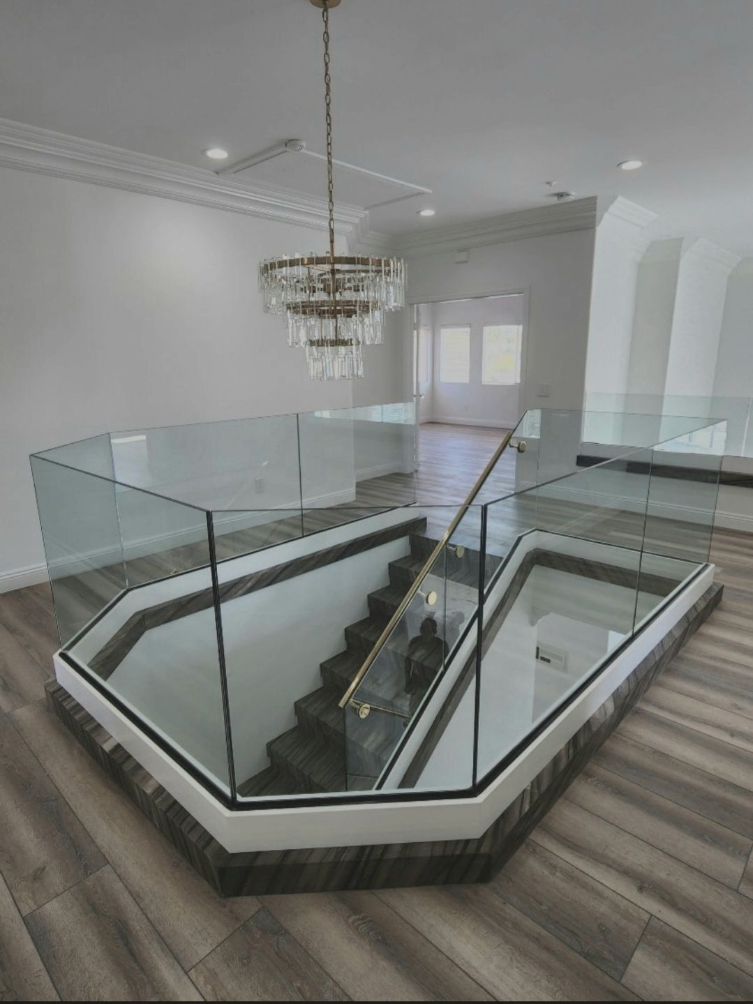 Staircase with glass railing, chandelier, and marble trim in a bright interior.