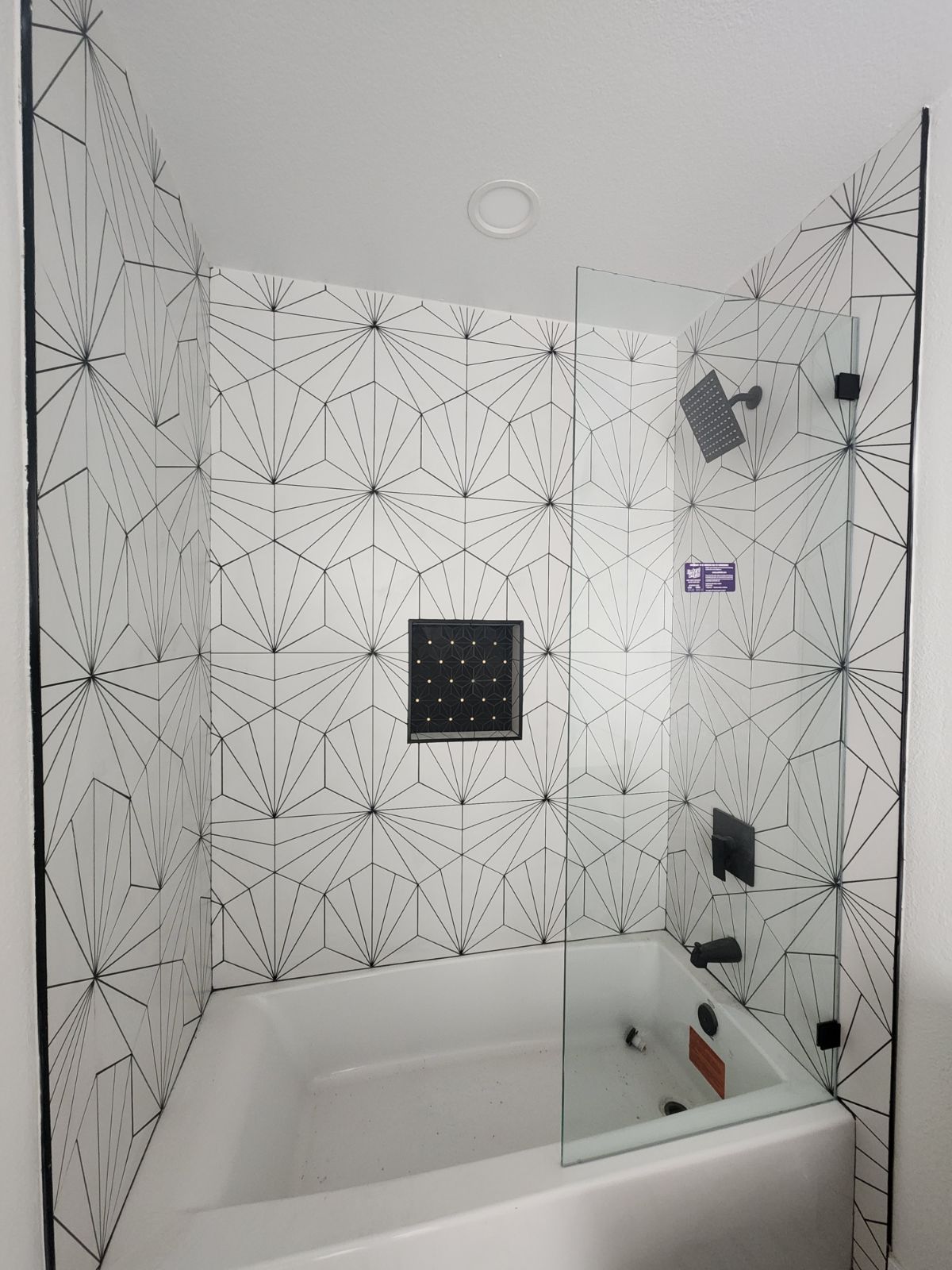 Bathroom with white and black geometric tile, a bathtub, and a glass shower screen.
