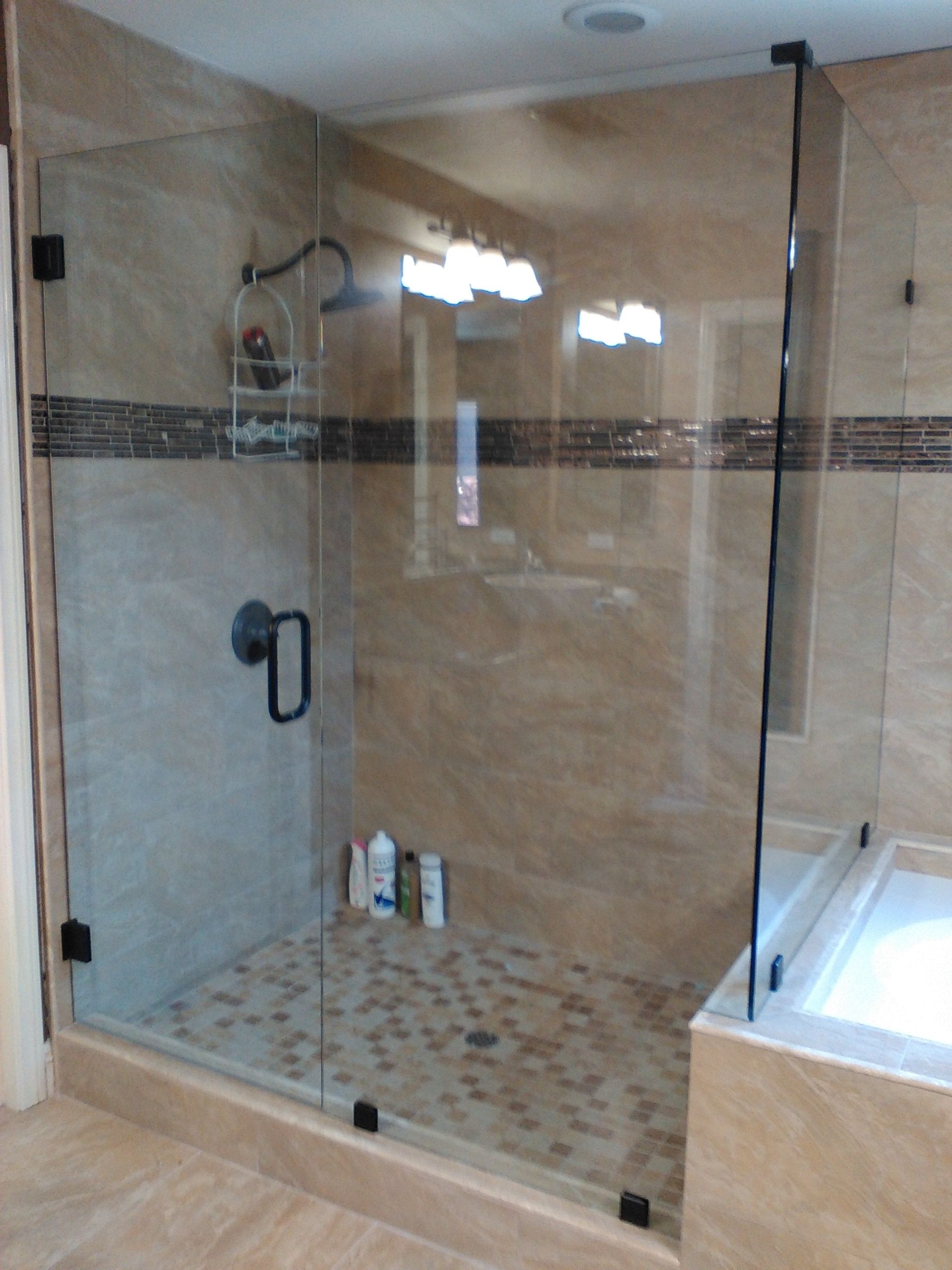 Glass-enclosed shower with stone tile floor and walls. Black hardware and a small shelf.