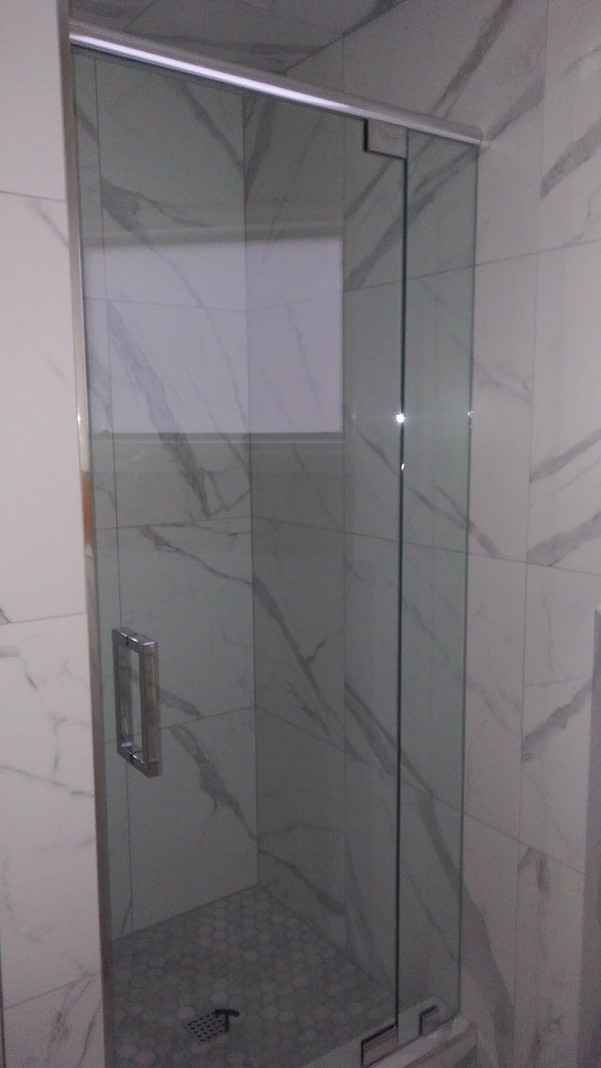 Glass shower door in a bathroom with marble-patterned tile walls.