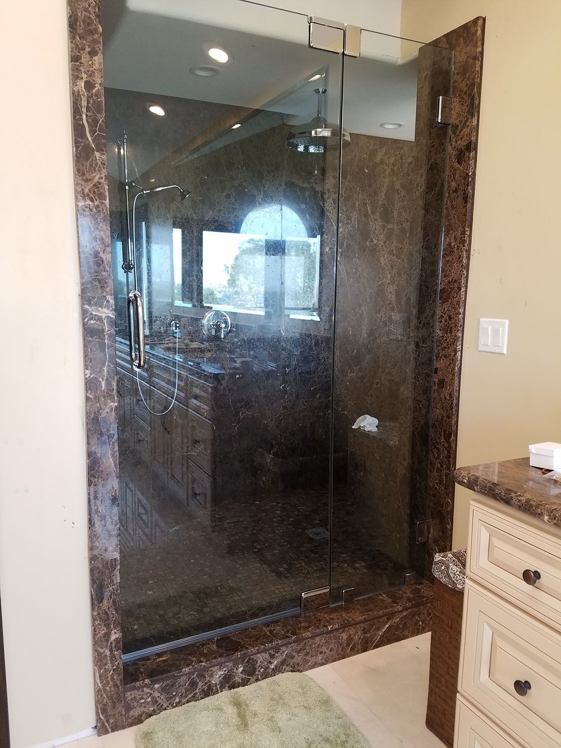 Brown marble-framed glass shower door in a bathroom with a marble countertop and cream-colored walls.