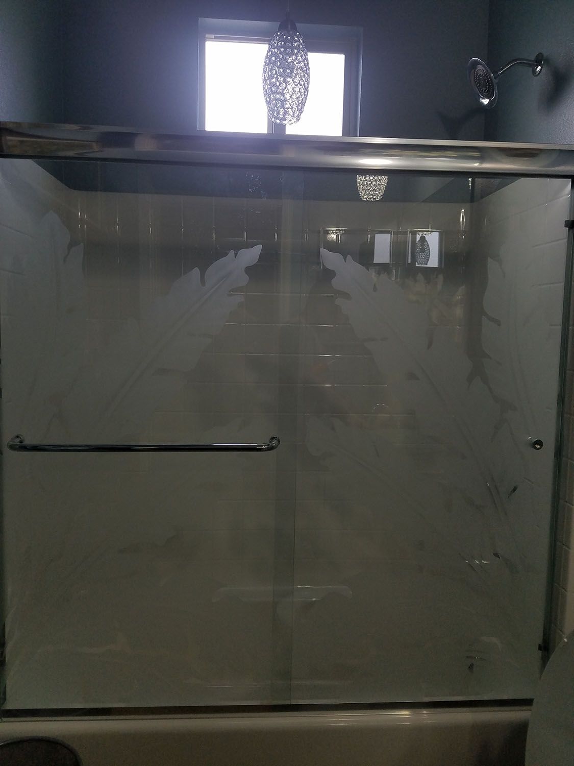 Shower with glass doors covered in condensation, with a window and shower head visible.