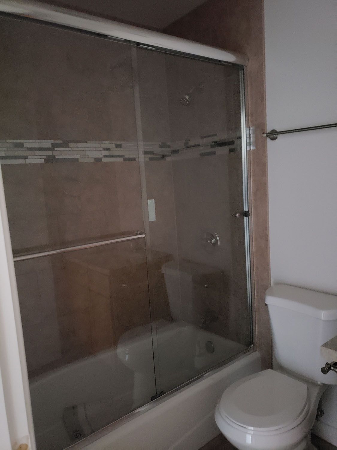 Bathroom with a shower/tub combo. Glass sliding door, tan tile, toilet, and towel rack.