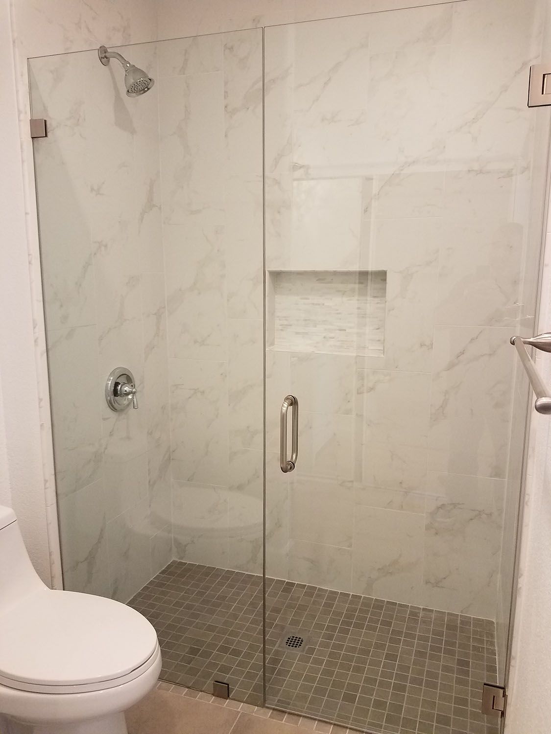 A modern bathroom with a glass shower enclosure and marble tile walls.