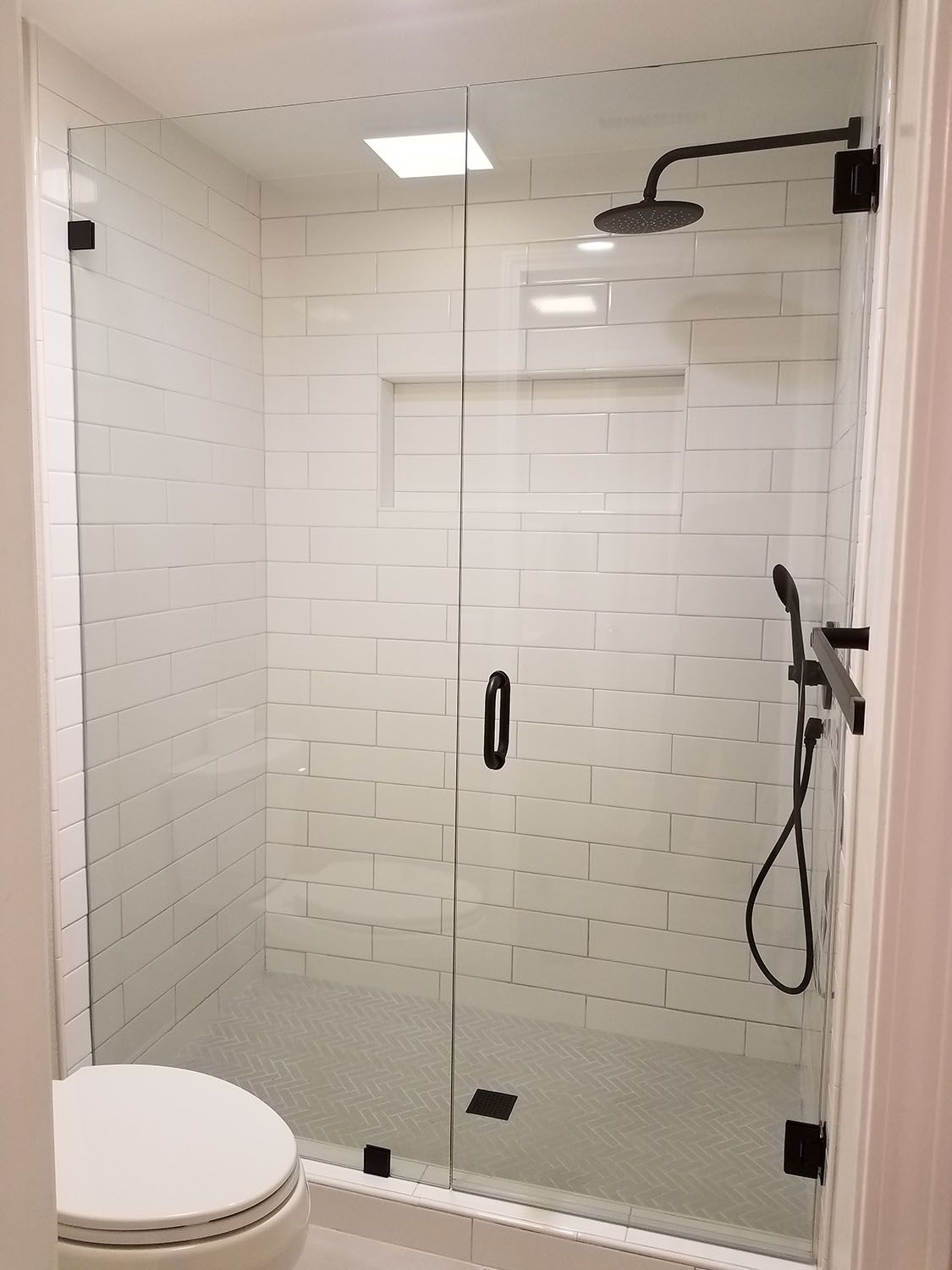 Glass shower with white subway tile walls, black fixtures, and a handheld shower.