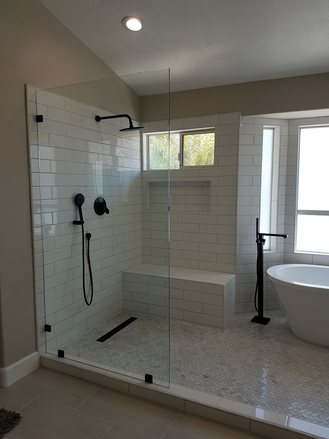 Modern bathroom with glass shower, subway tile walls, black fixtures, and a freestanding tub.