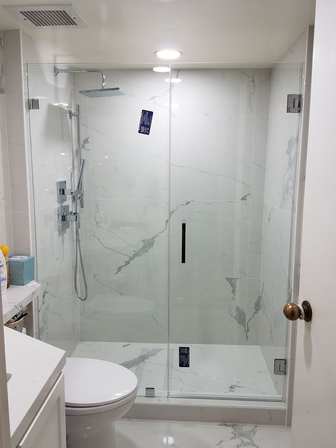 Modern white marble-tiled shower with glass doors and chrome fixtures.