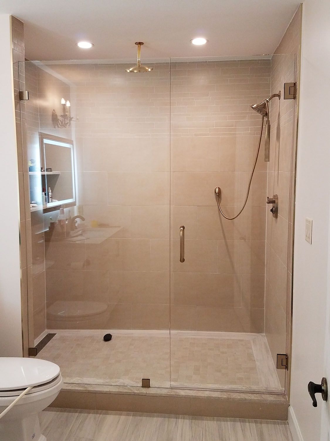 Modern bathroom with glass shower enclosure, beige tiles, and silver fixtures.