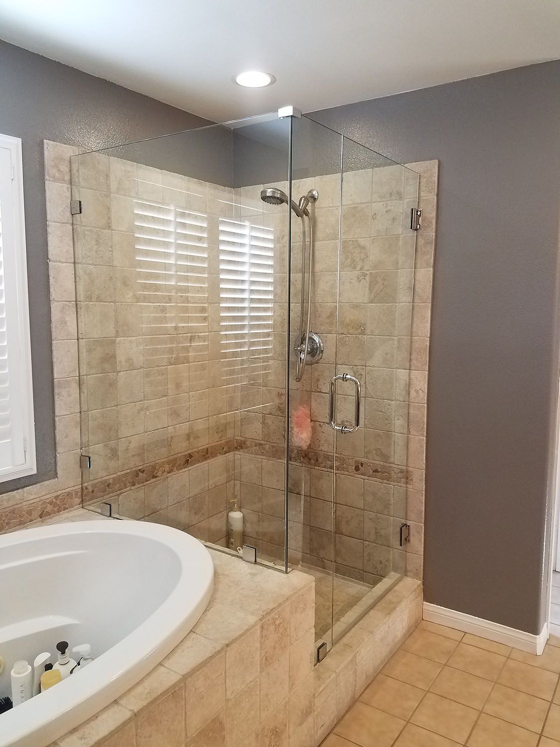 Bathroom with glass shower, tan tile, white tub, and gray walls.