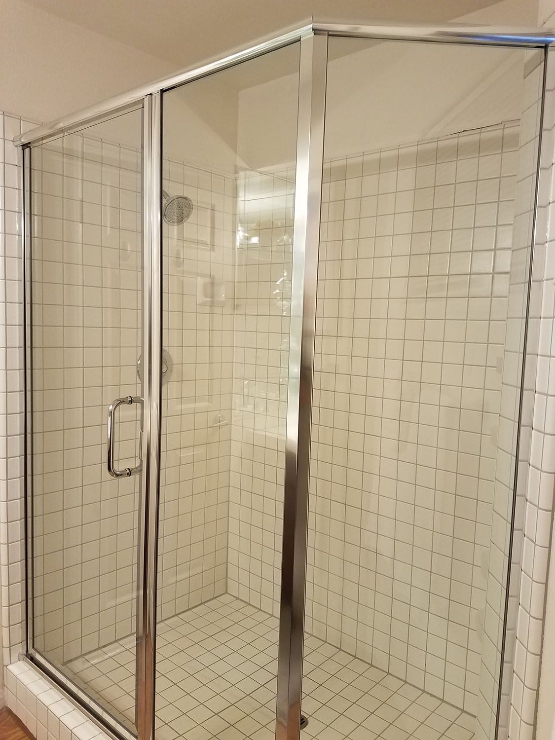 Glass shower enclosure with white tiled walls and silver frame.