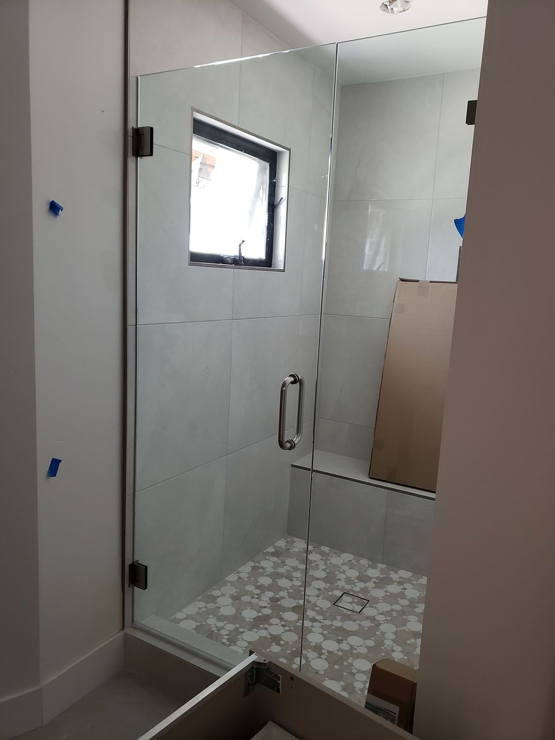 Glass shower enclosure with black hinges and handle, white tiled walls, and patterned floor.