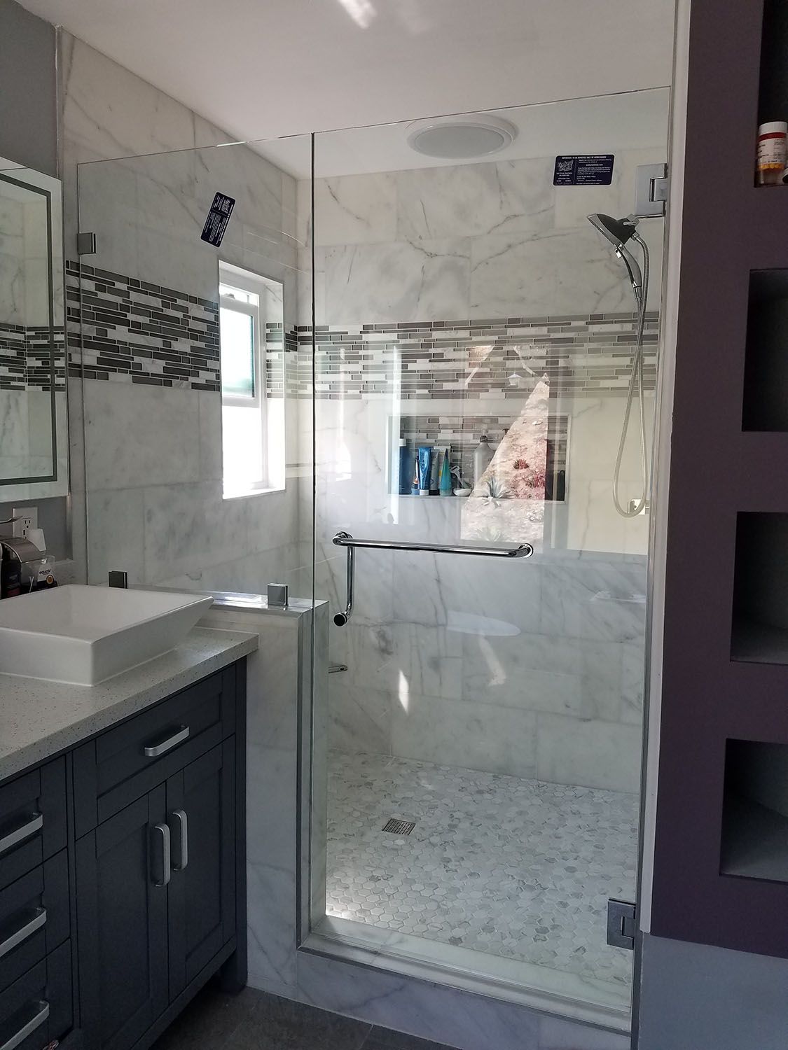 Modern bathroom with glass shower door, marble tile walls, and gray vanity.