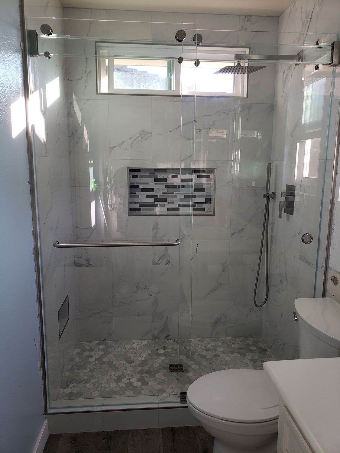 Modern bathroom with marble tile shower, glass door, and toilet.