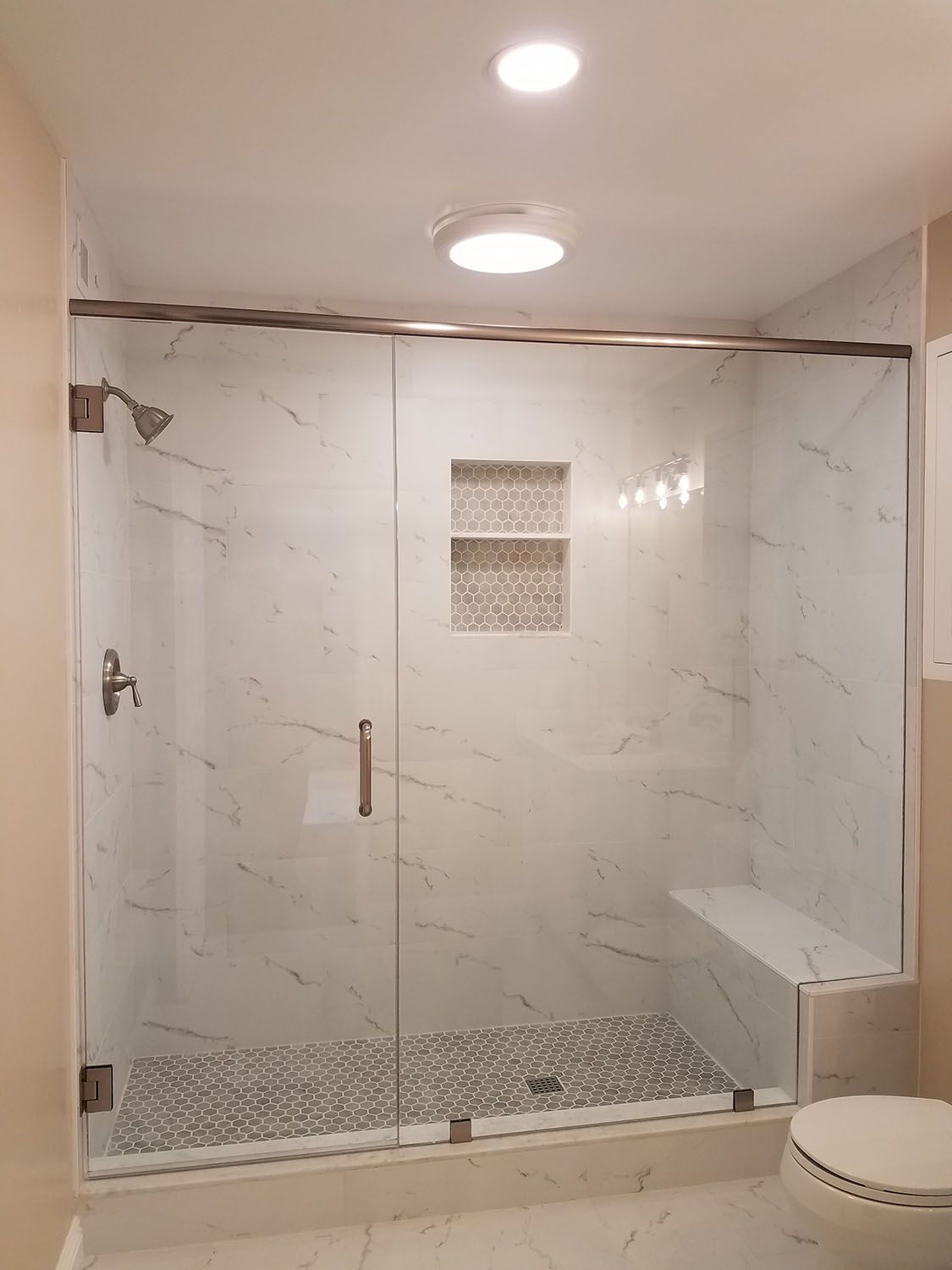 Glass-enclosed shower with marble tile walls, pebble floor, built-in seat, and recessed shelf.