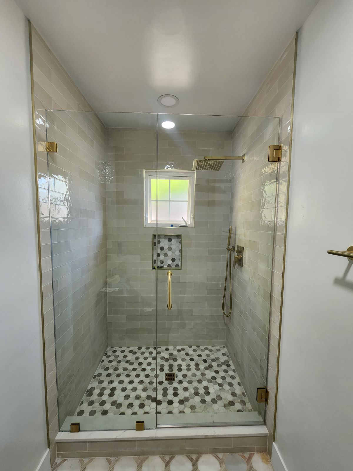 Modern shower with glass doors, gold fixtures, and light-colored tile.