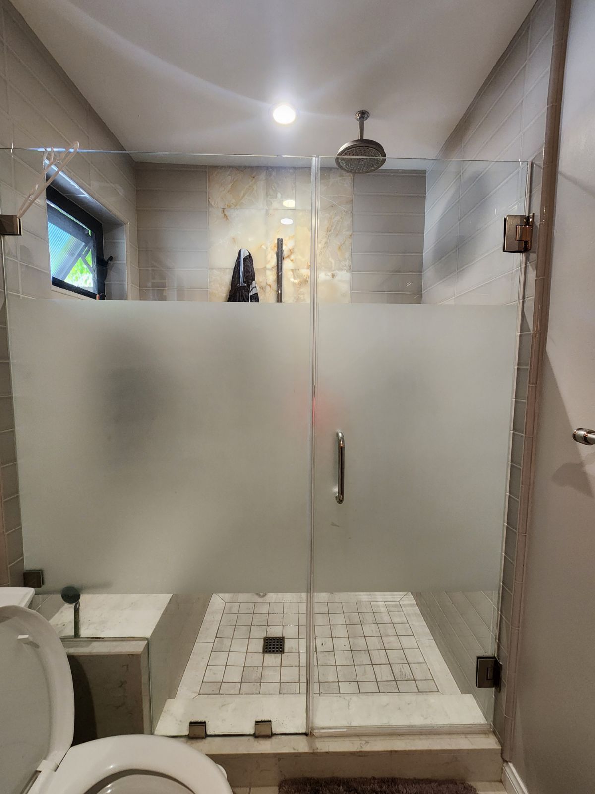 Bathroom with frosted glass shower doors, tan tile walls, and a toilet.