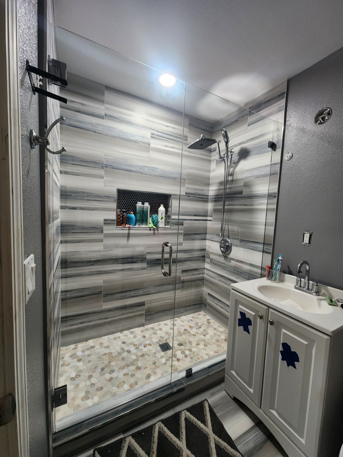 Modern bathroom with gray and white tile shower, glass door, and white vanity.