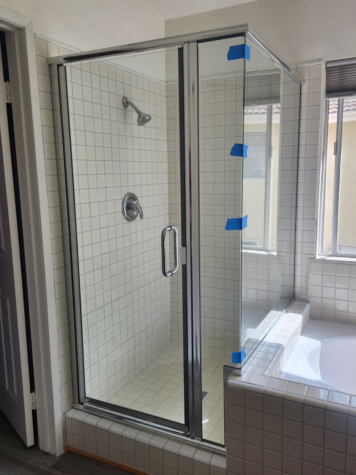 A glass shower enclosure with chrome trim against white tile walls, a silver shower head and fixtures.