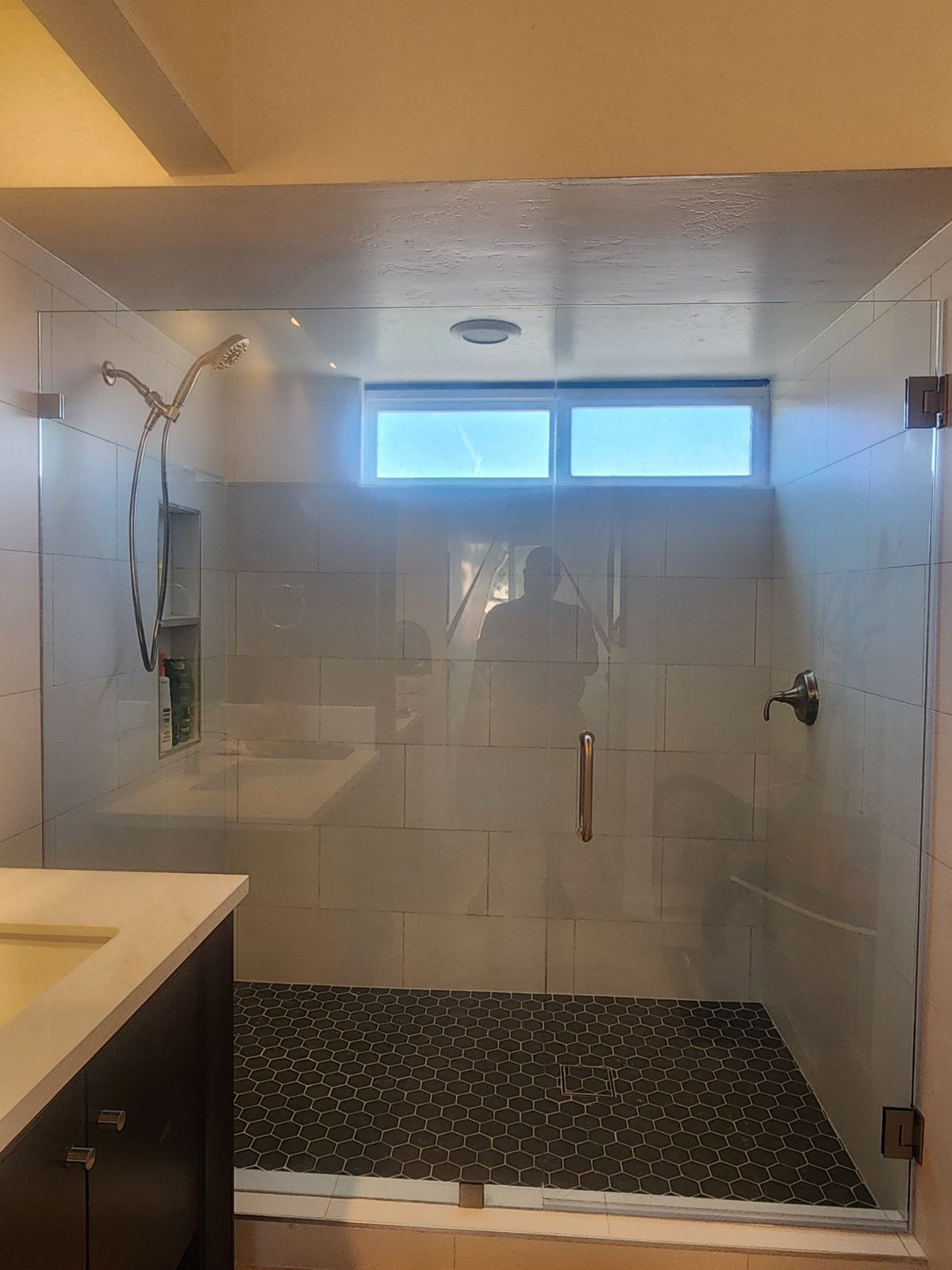 Glass shower with dark floor, white tiled walls, and small window.