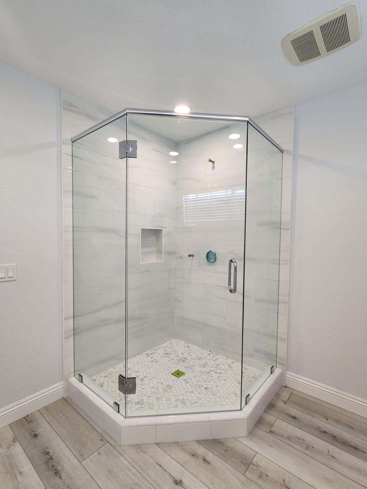 A newly remodeled corner shower with clear glass doors and marble-like tile.