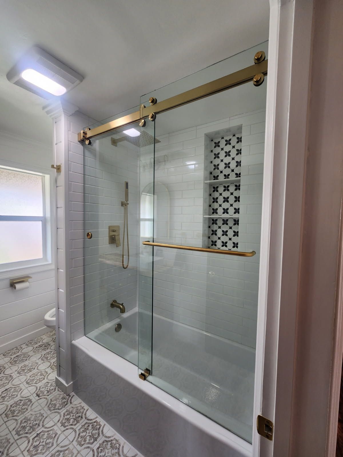 Bathroom with glass shower doors and gold hardware, white and patterned tile.