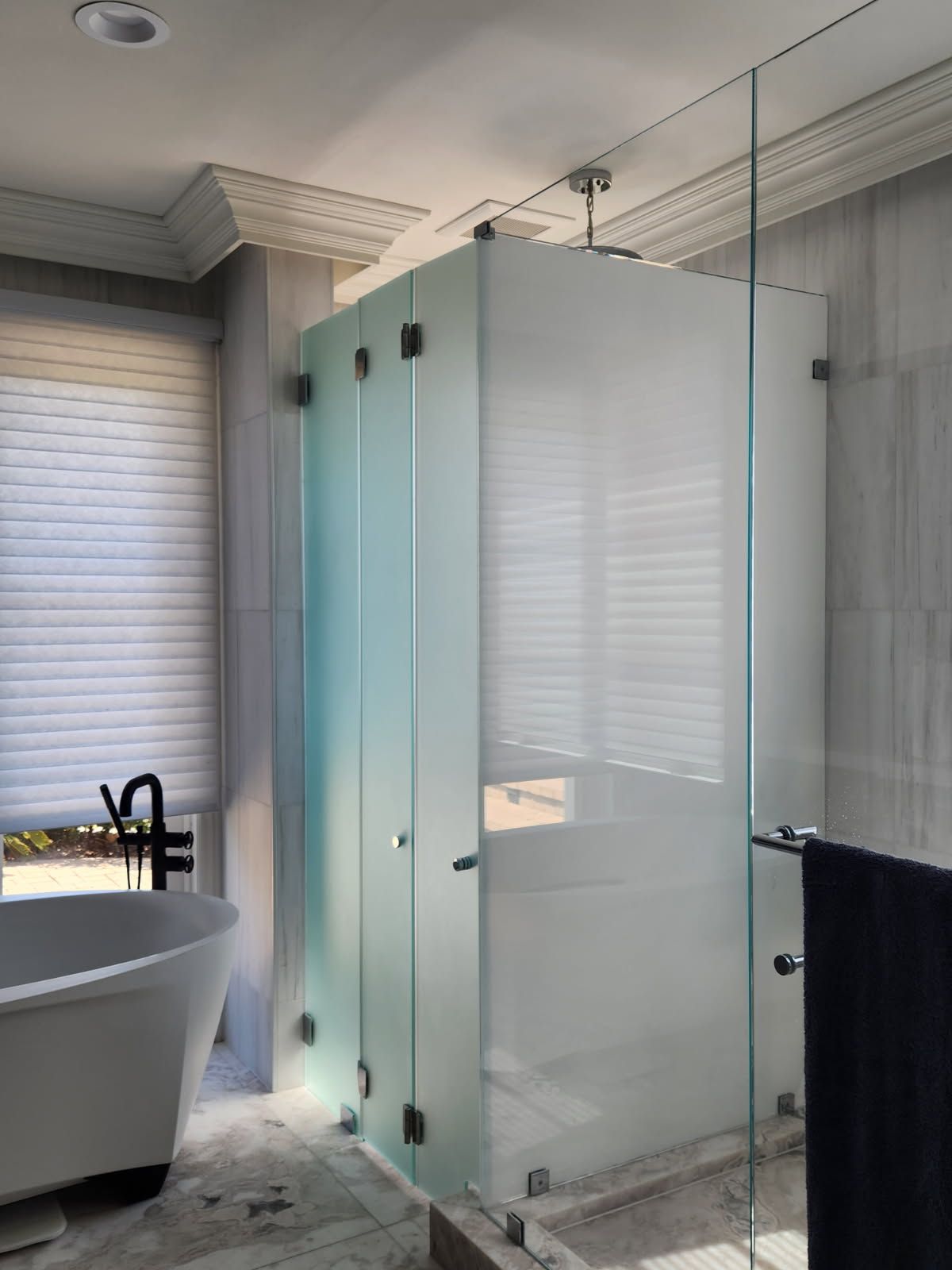 Frosted glass shower enclosure in a bathroom with a soaking tub and window with blinds.