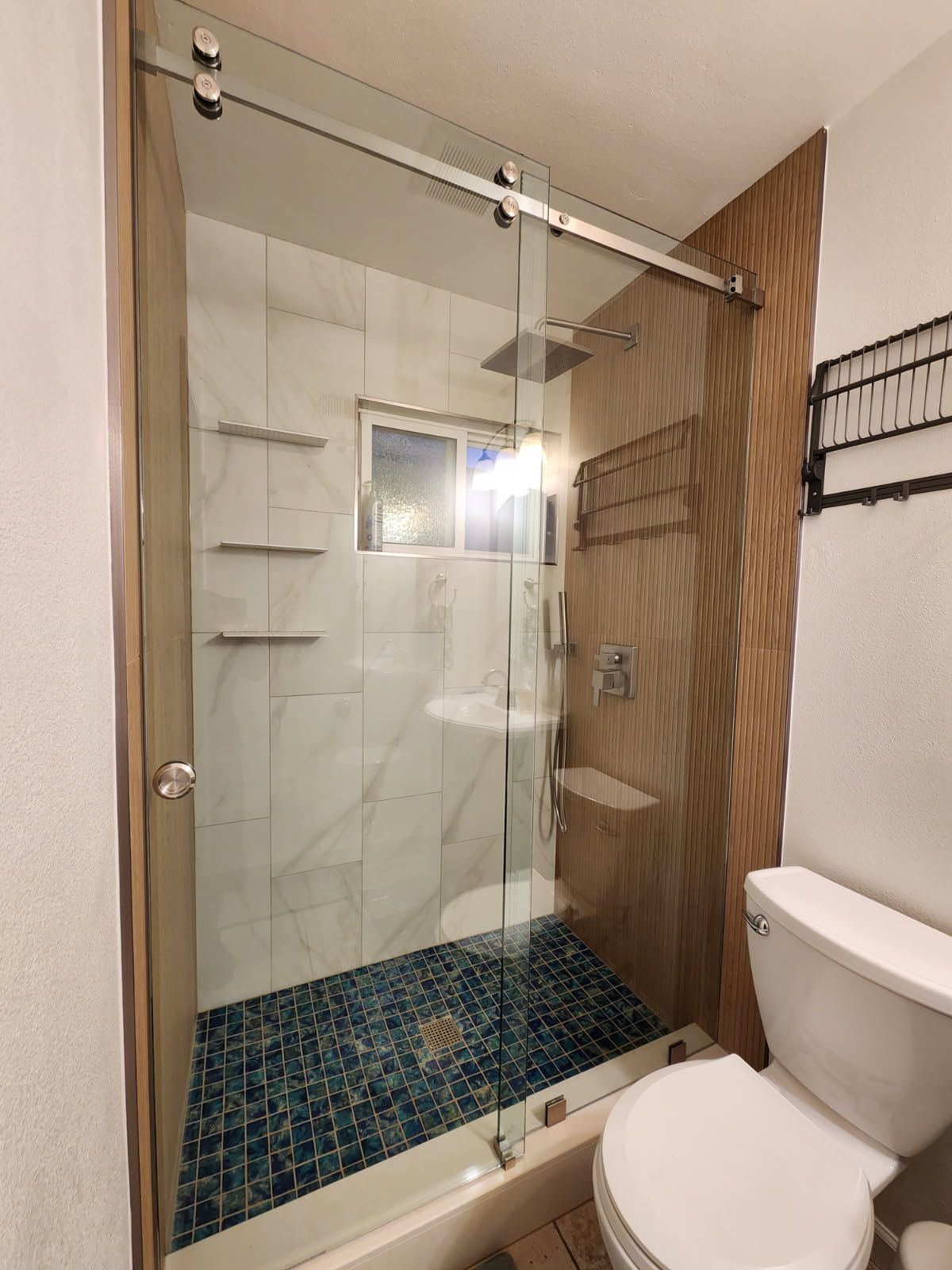 Shower with sliding glass doors, blue tile floor, white marble tile walls, and a toilet.